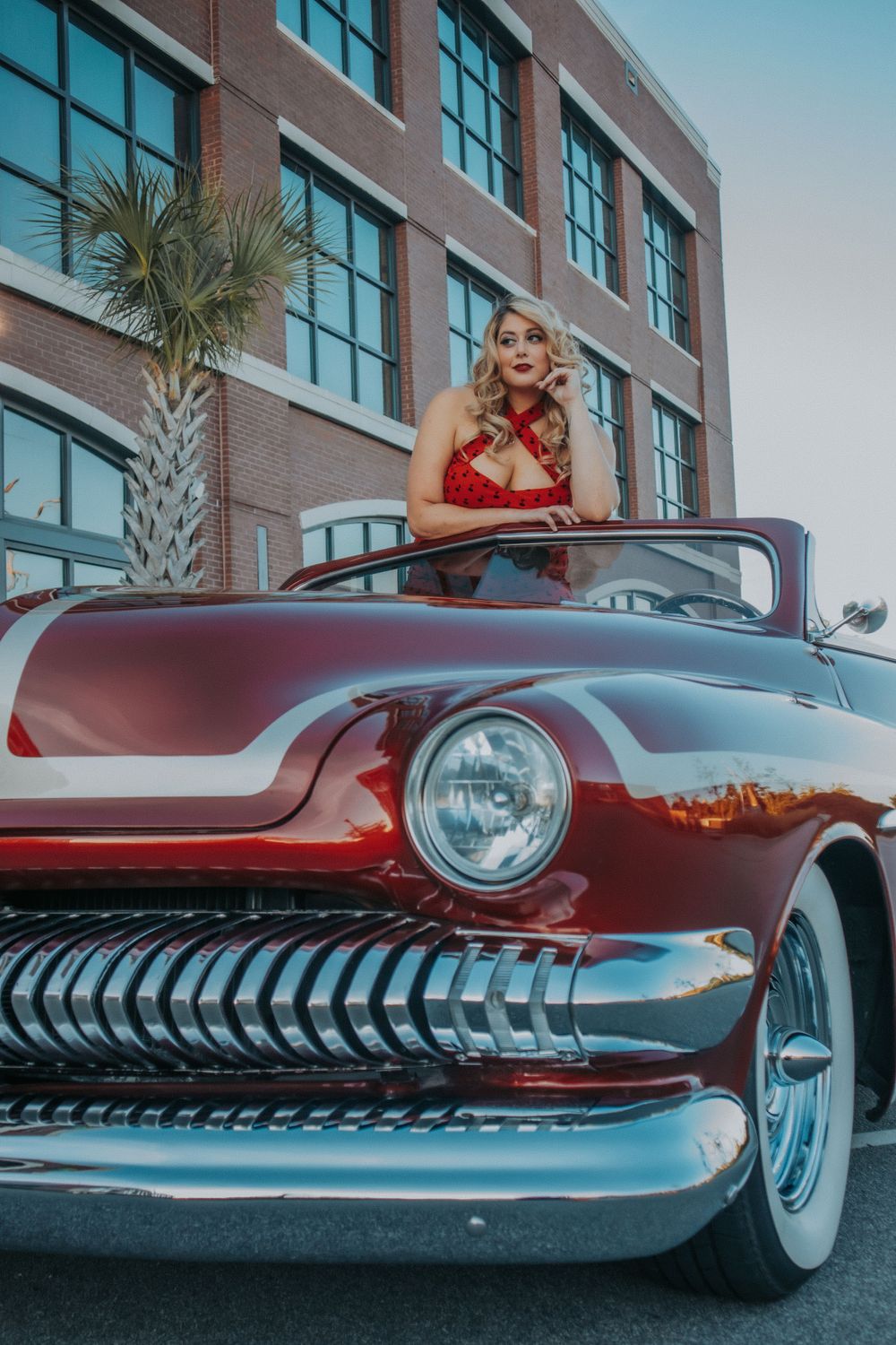A woman poses inside a red vintage car
