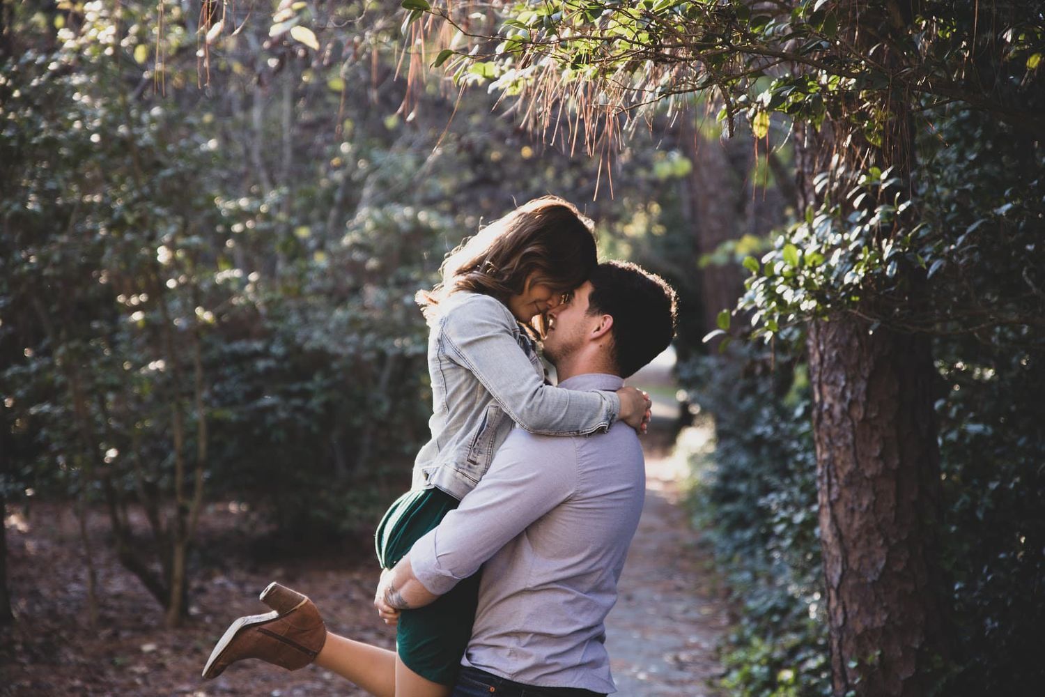 Romantic embrace on woodland path with sunlight filtering through trees.