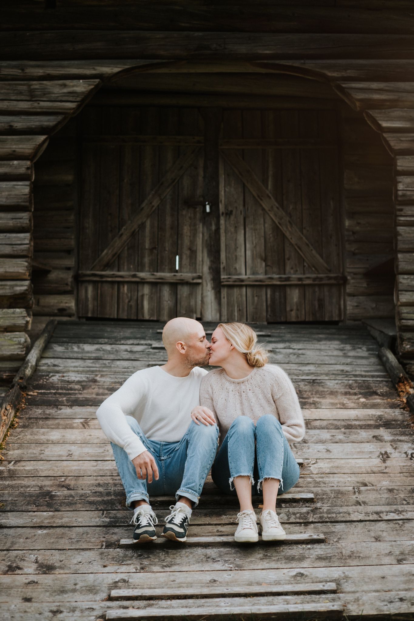 Couple sitting together on wooden porch steps of rustic barn sharing an intimate moment.