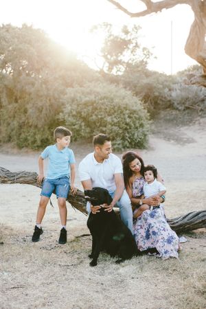 Family relaxing together on fallen tree trunk with their black dog.