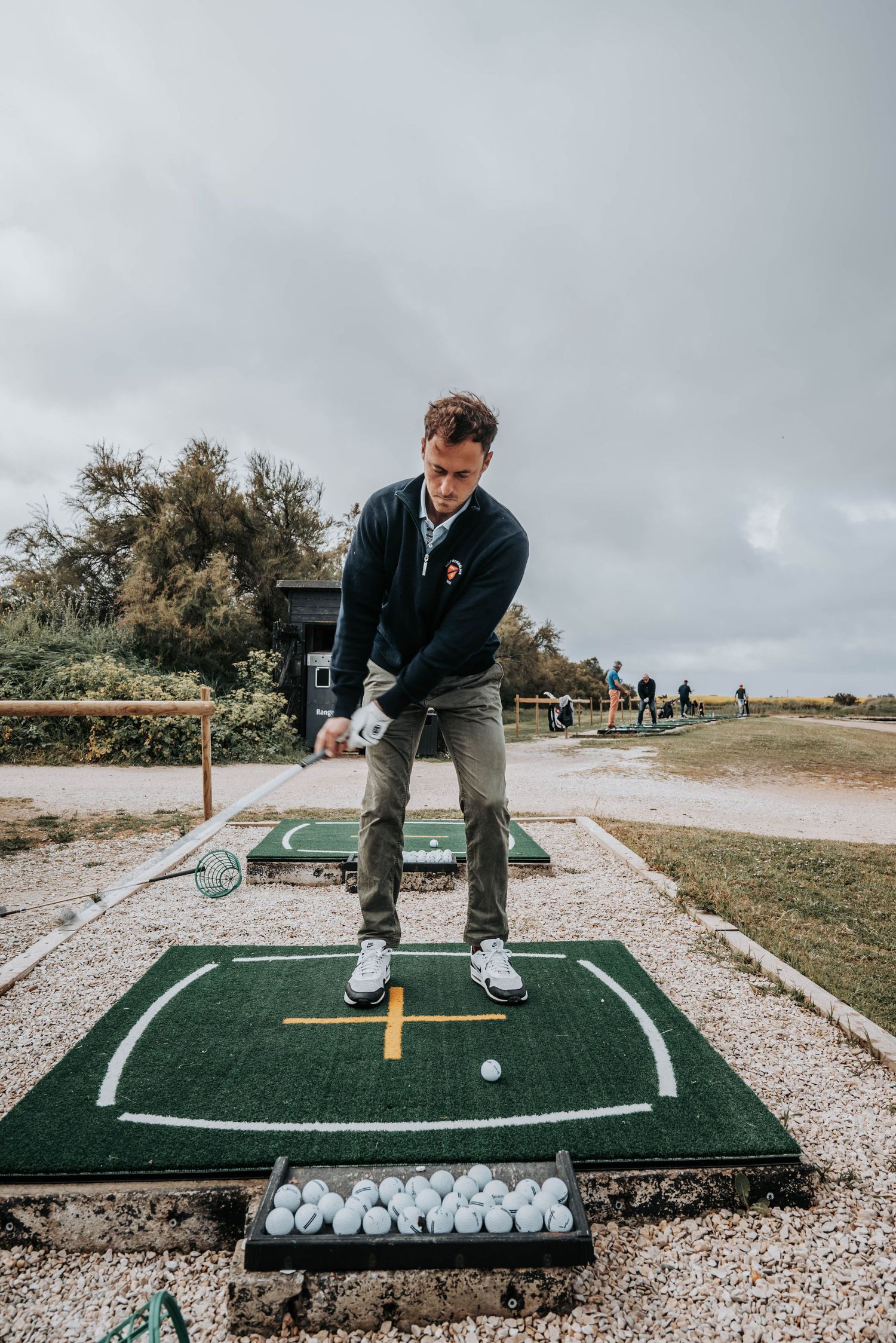 Golfer setting up to practice their swing on an outdoor driving range mat with golf balls lined up.
