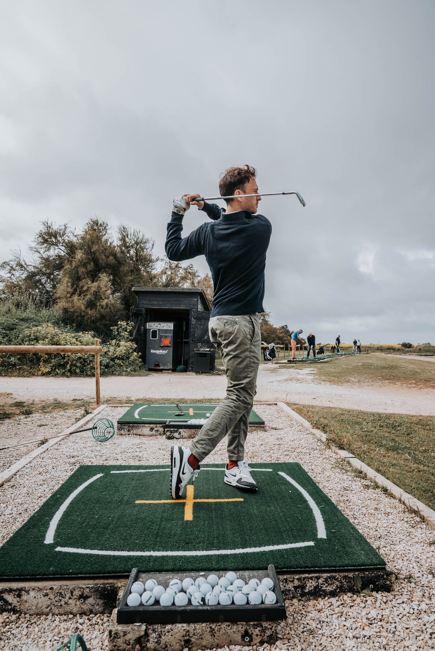 Golf practice session showing proper backswing form on outdoor training mat.
