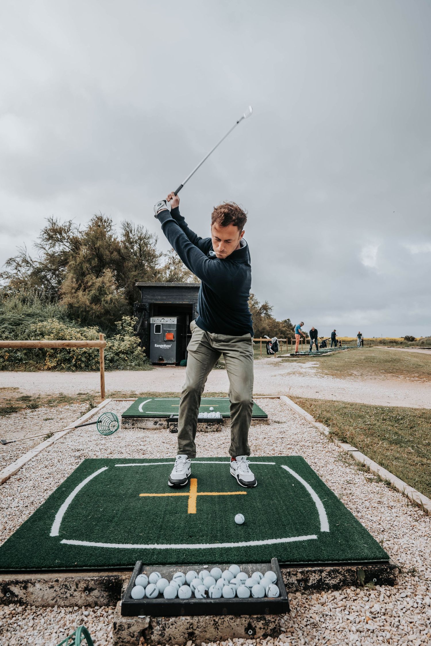 Golfer reaching the top of their backswing on a practice mat at an outdoor facility.