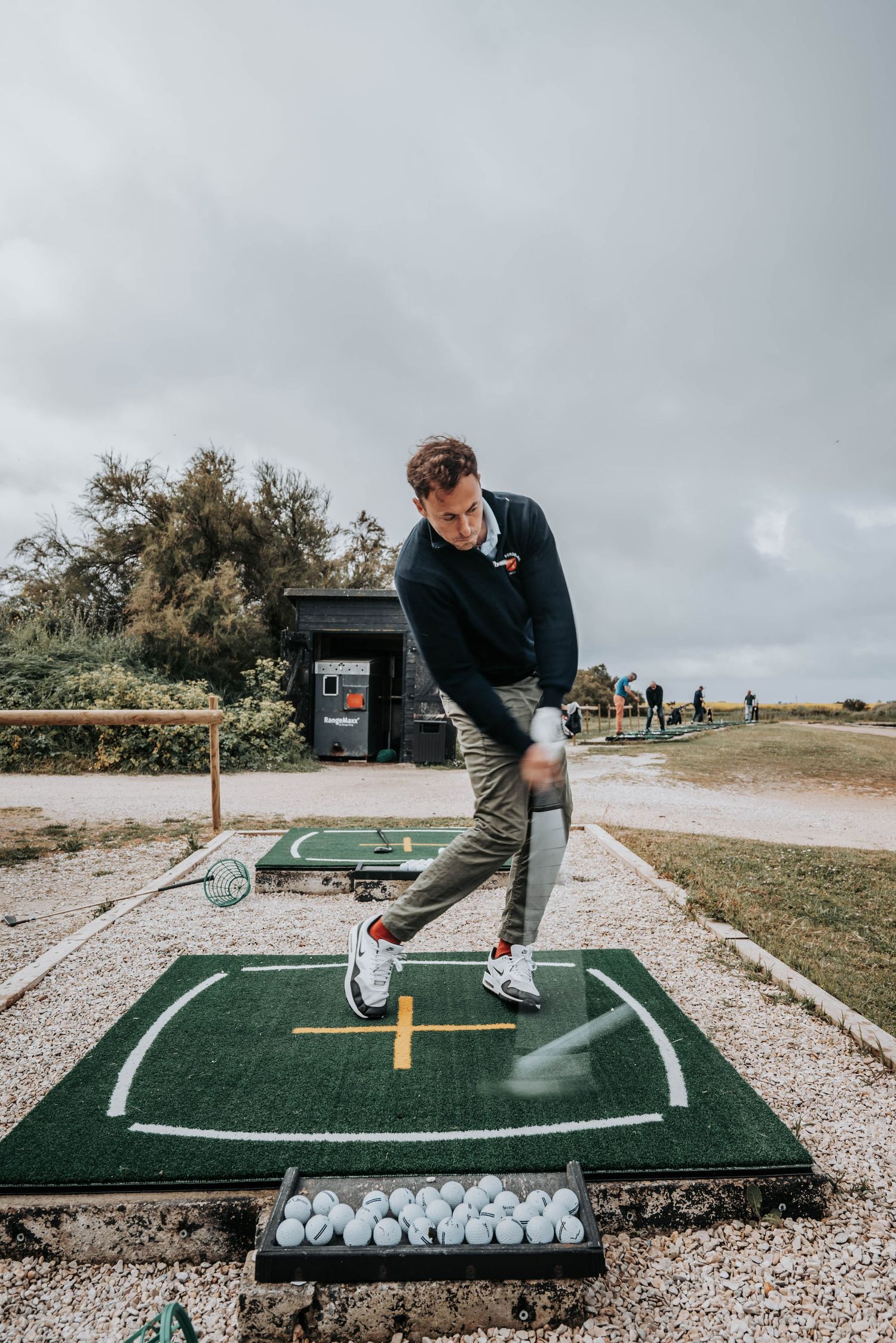 Golfer in follow-through position practicing on a synthetic turf mat with golf balls nearby.