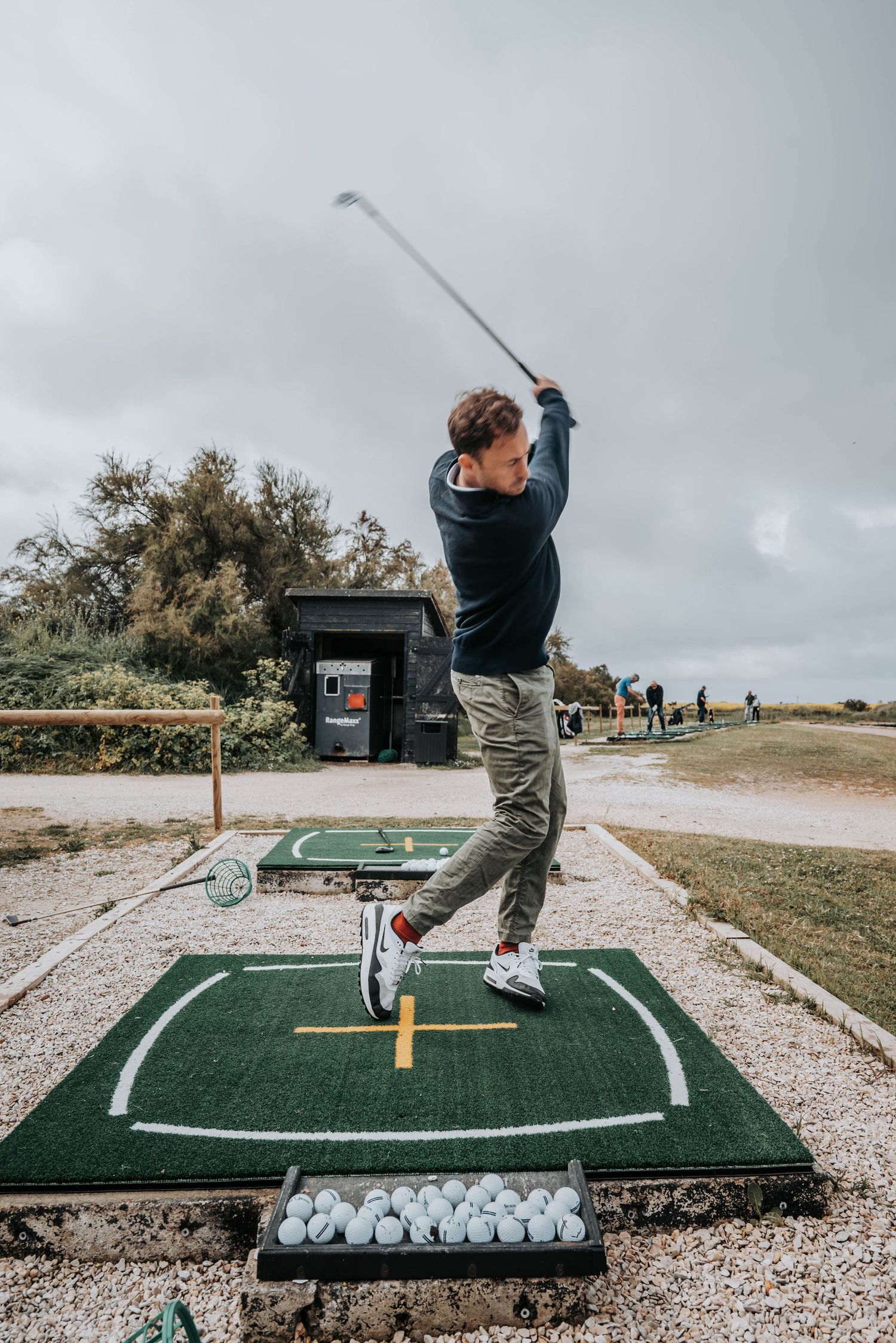 Golfer executing swing sequence on outdoor practice mat with collection of practice balls visible.
