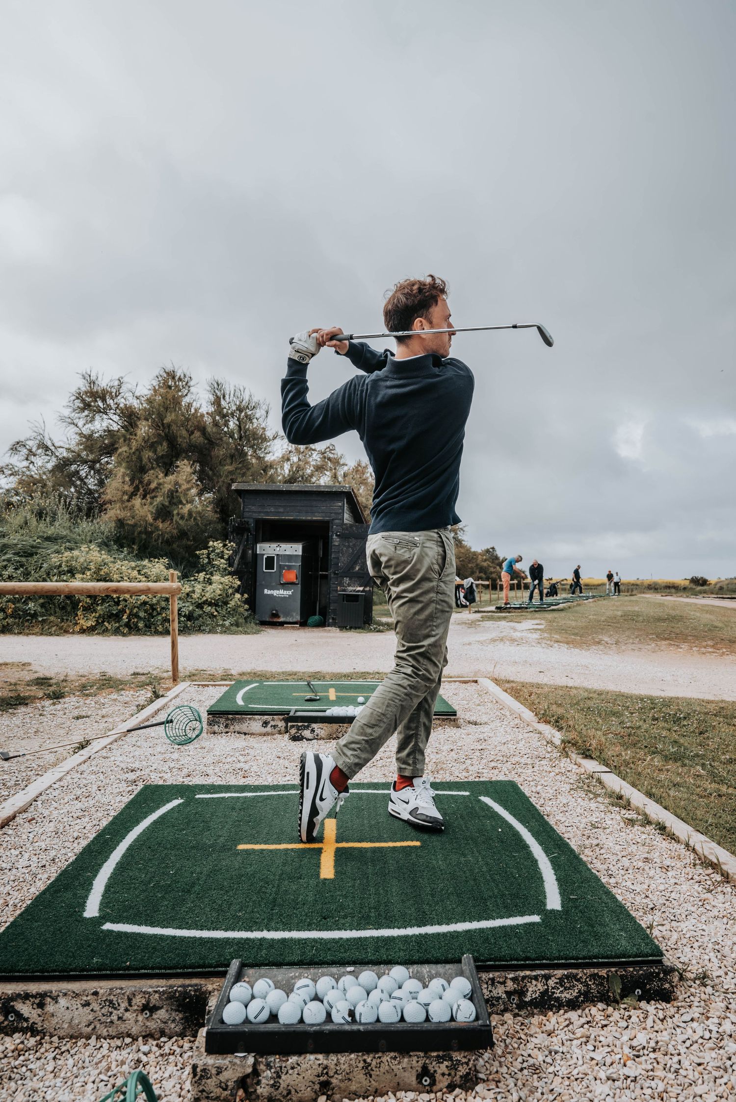 Golf swing demonstration showing proper form on practice mat with balls ready.