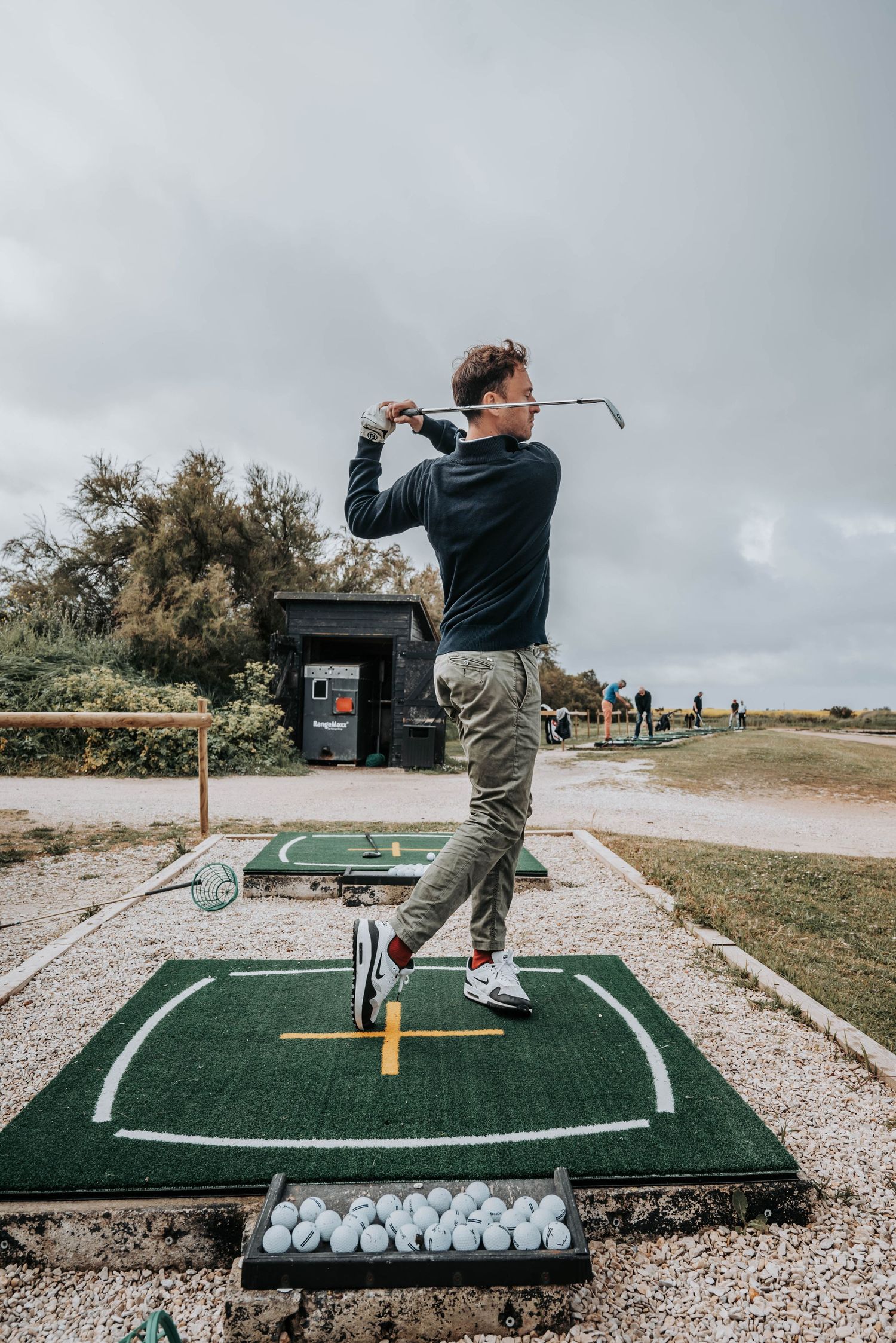 Golfer practicing proper swing mechanics on outdoor mat with practice balls visible.