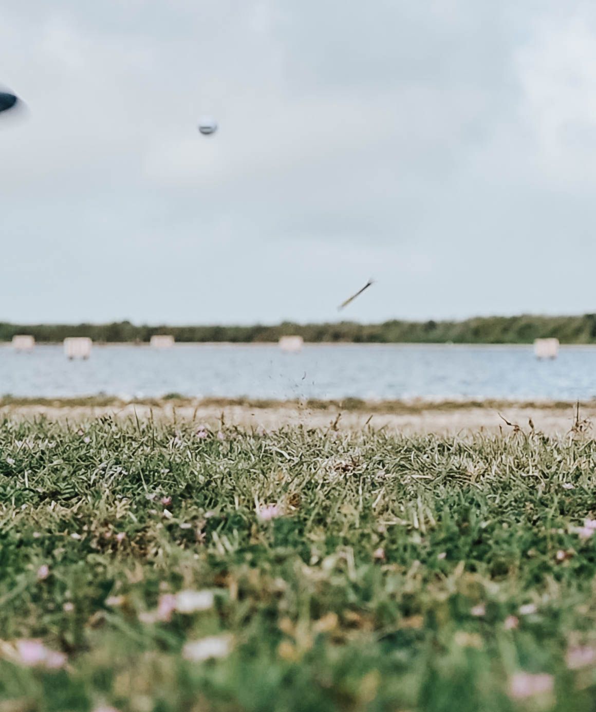 Golf ball in mid-flight over grassy course with water hazard in background.