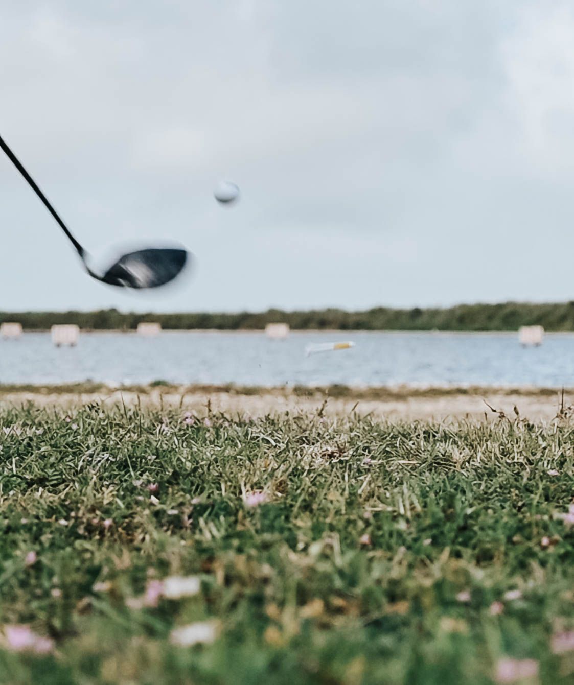 Action shot of golf ball being launched from tee with club head in motion.