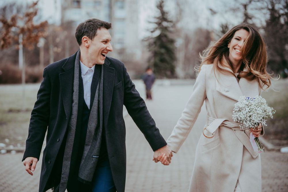 Couple walking and laughing together outdoors while holding hands on a fall day.