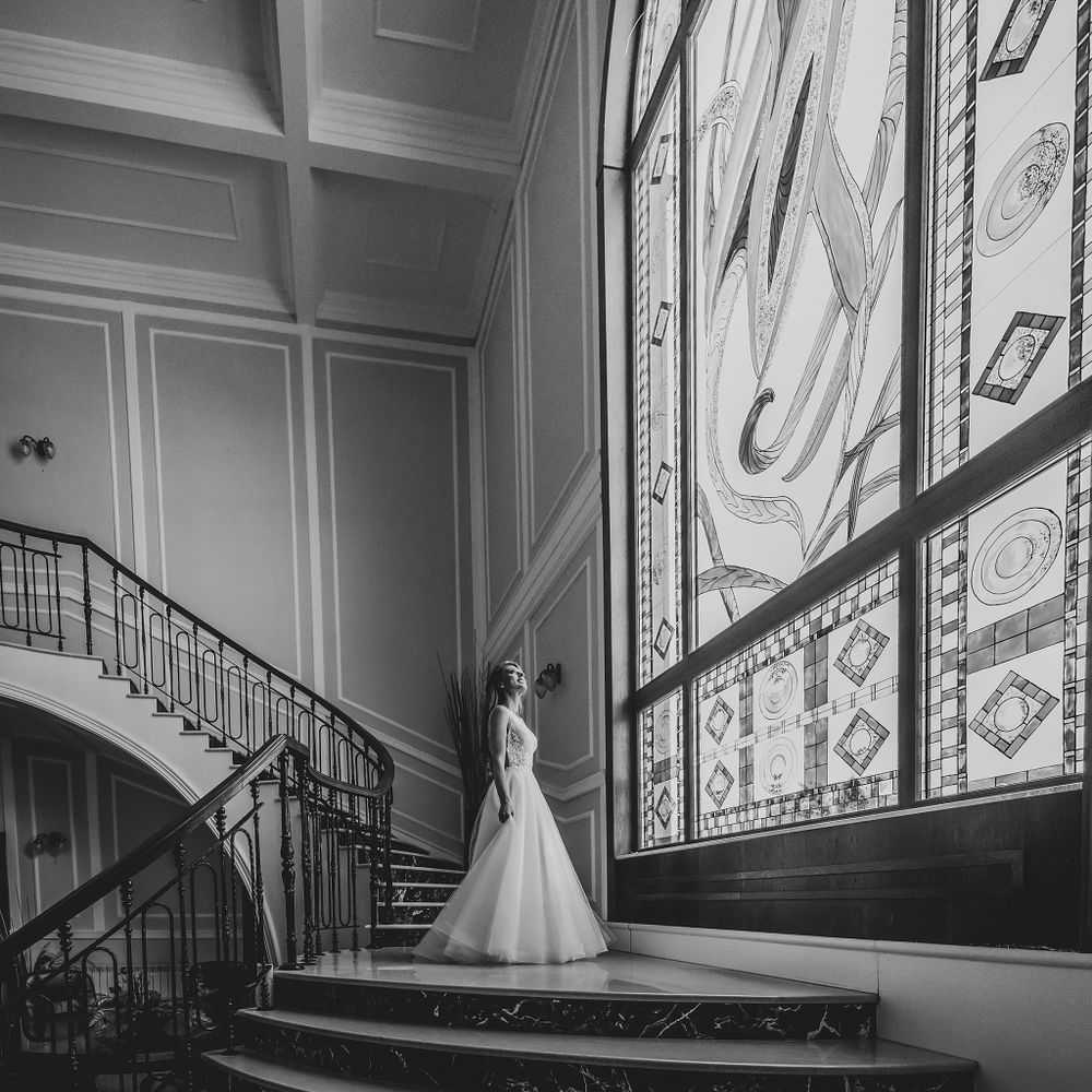 Elegant bridal portrait on grand staircase next to ornate stained glass windows.