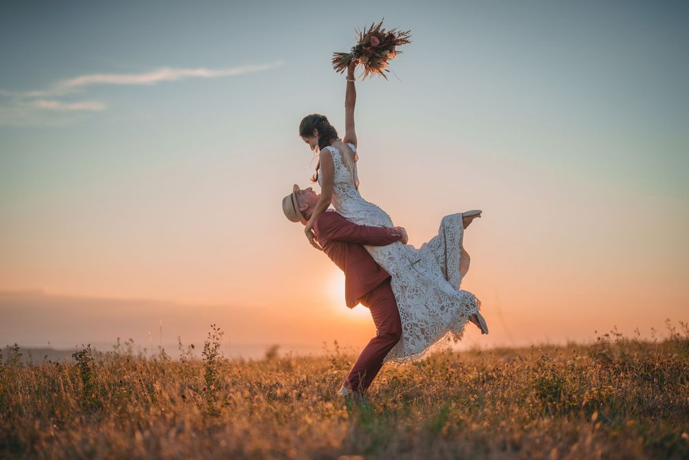 A figure in a white dress dances joyfully in a field at sunset while holding a flower bouquet.