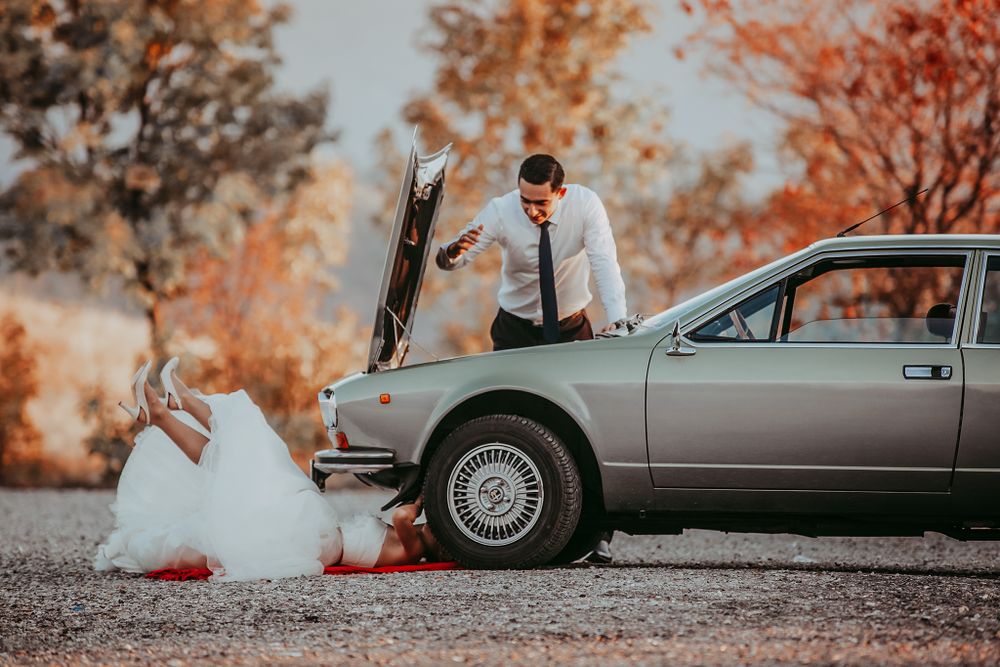 Creative wedding photo showing couple playfully pretending to fix broken down vintage car.