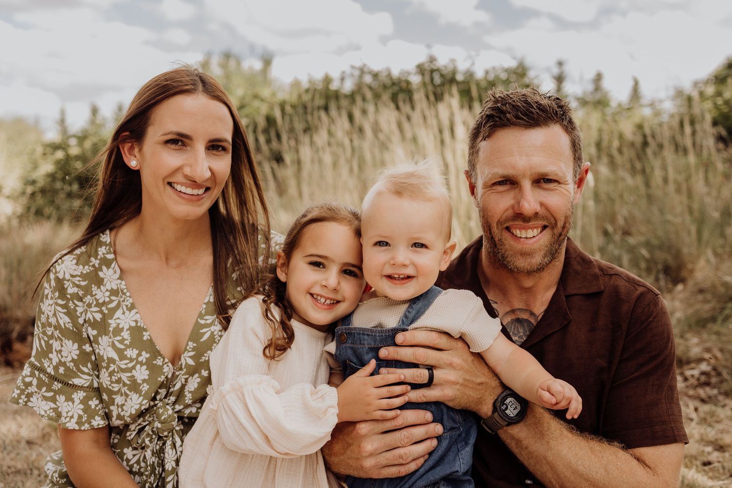 Candid family portrait outdoors with tall grass and natural lighting.