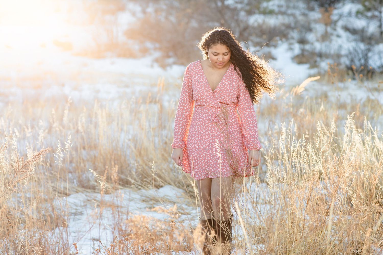Teen girl walks through grass and snow as the sun sets in Colorado Springs, Colorado.