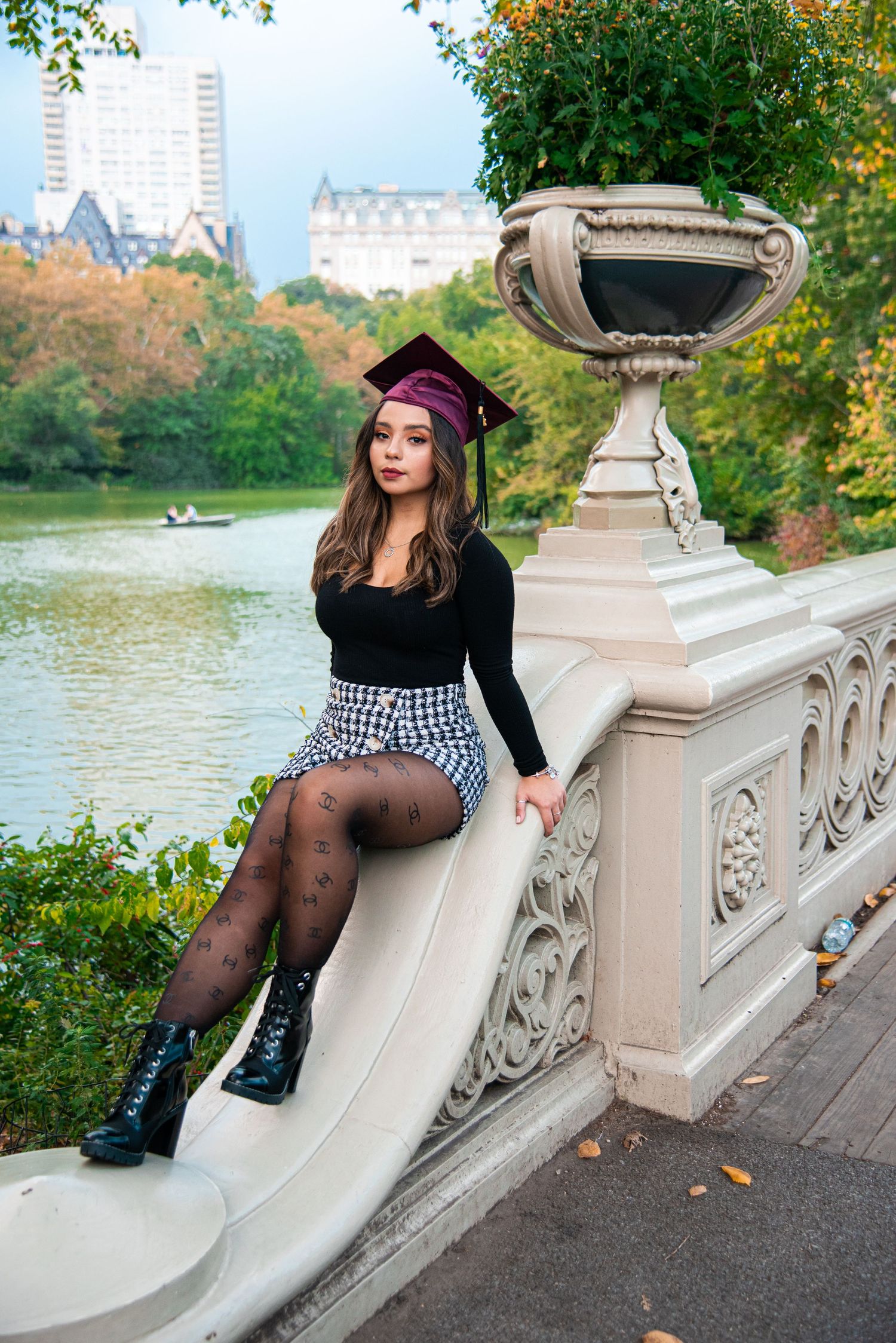 A graduation photo at Central Park bridge with fall foliage and lake in background.