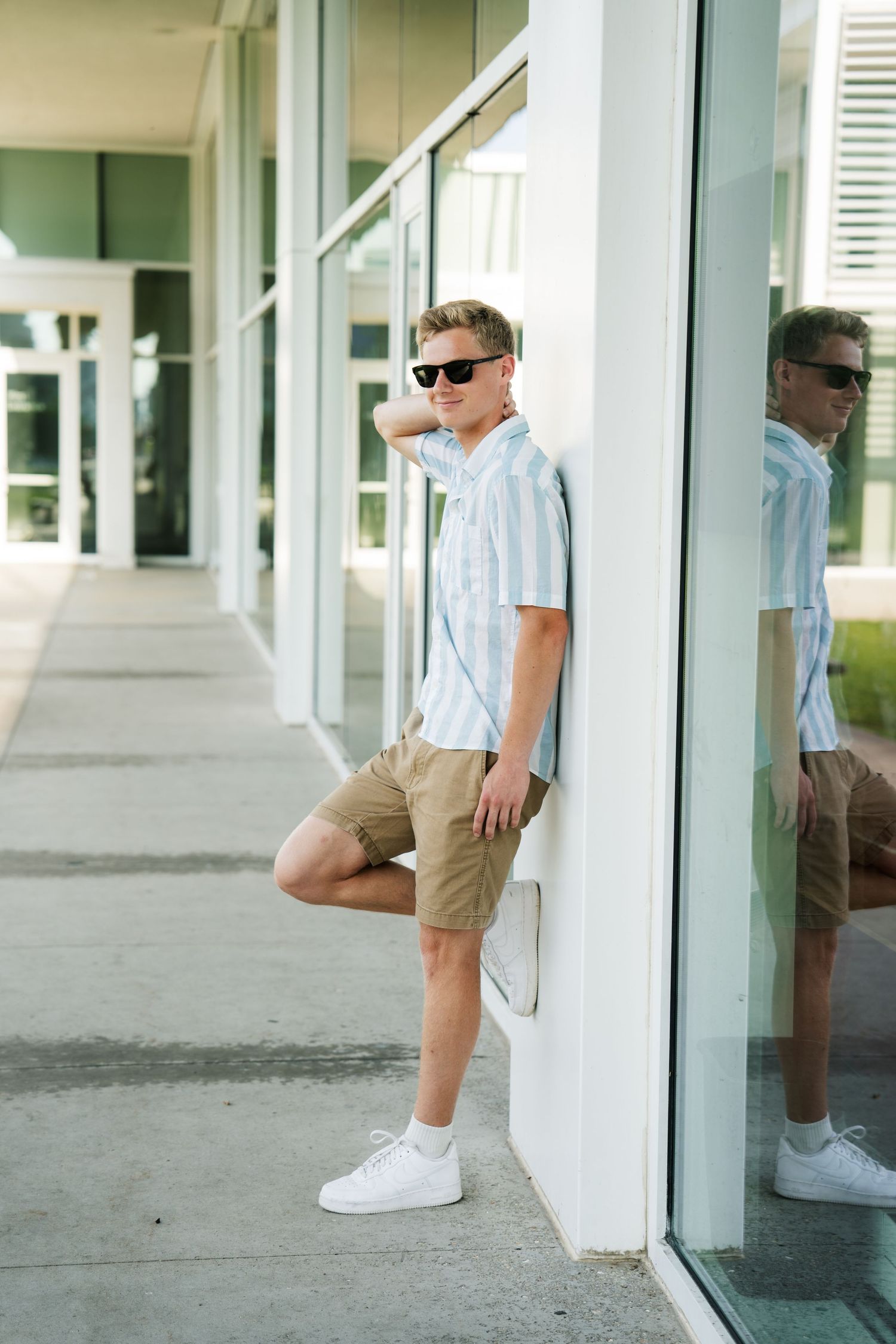 Senior portrait of boy in sunglasses smiling, leaning against white wall, shot by Milwaukee senior photographer Rachel Dickman.