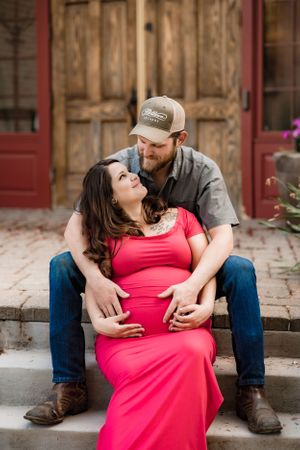 A couple shares an intimate moment on rustic steps with wooden doors in the background.