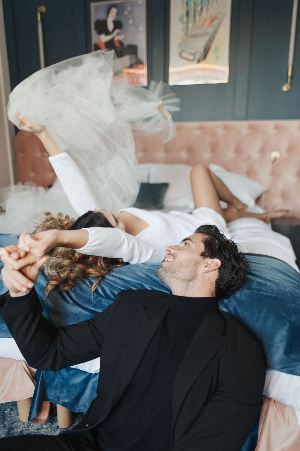 Playful couple lying on a blue sofa with flowing white tulle fabric.