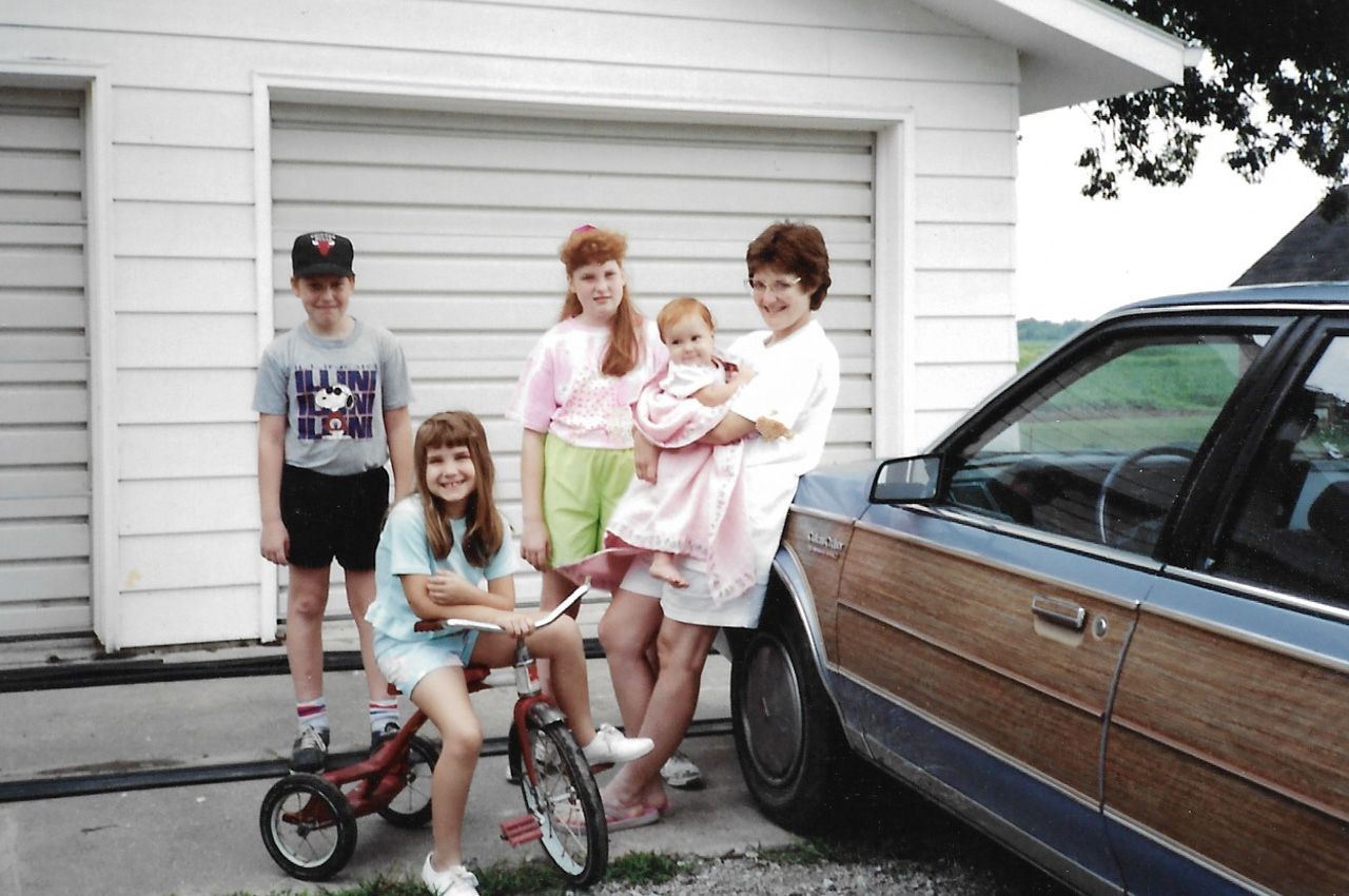 A casual group photo outside a white garage with a bicycle and classic car visible.