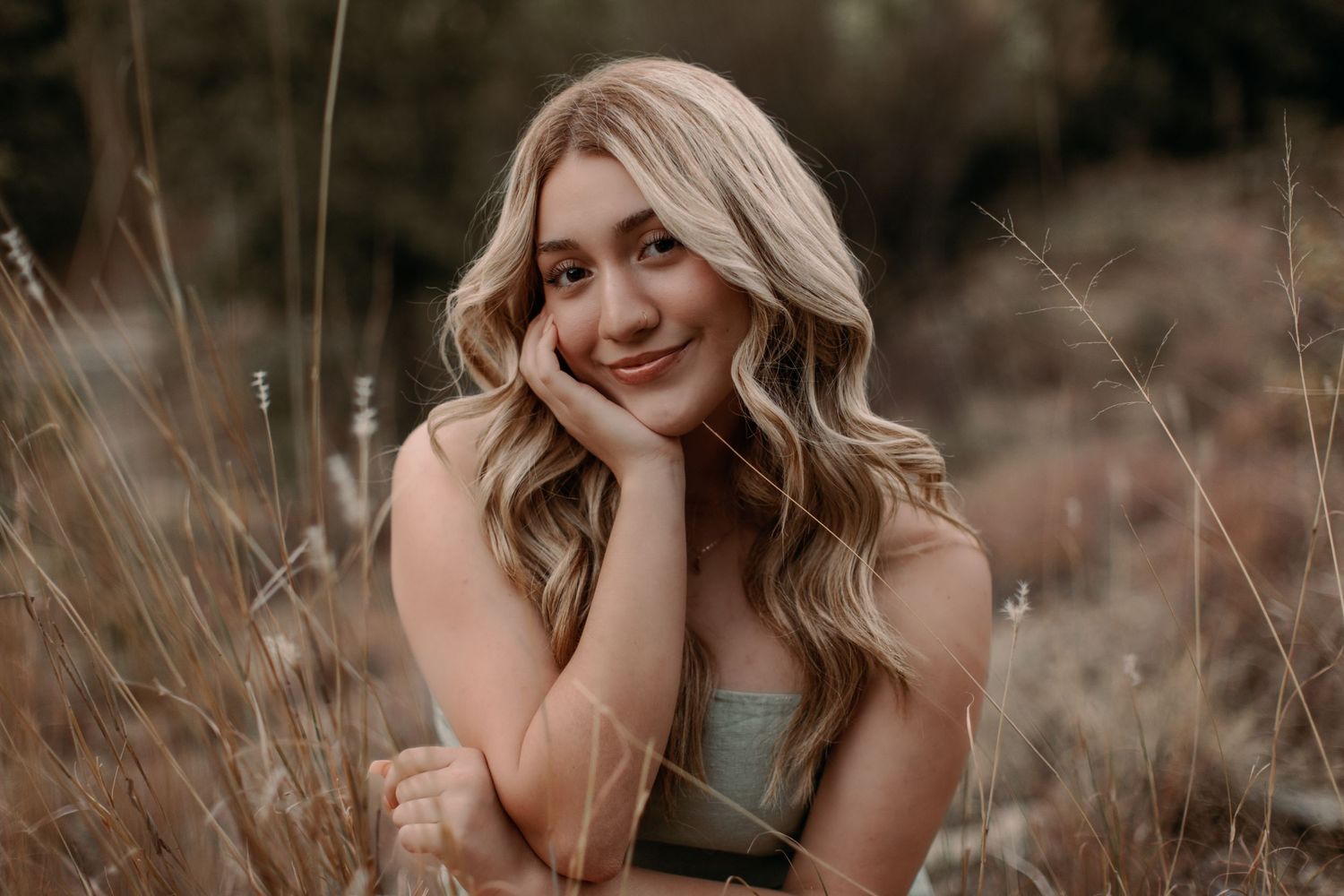 Tucson senior portrait of a teen girl posing in tall grass with warm natural light and a soft, confident smile.