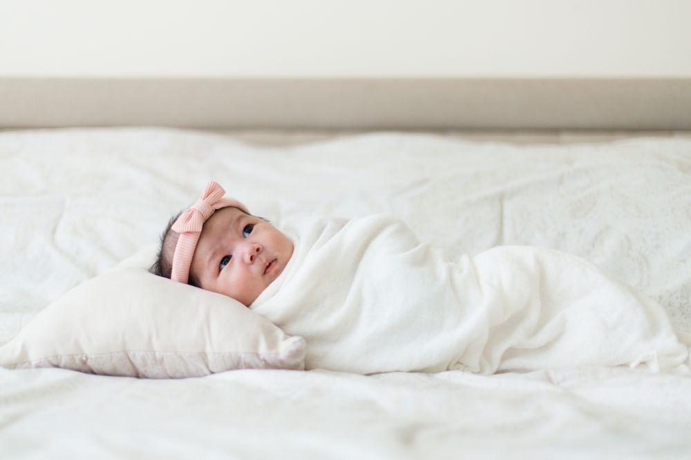 Newborn baby wrapped in white blankets lying peacefully on bed.