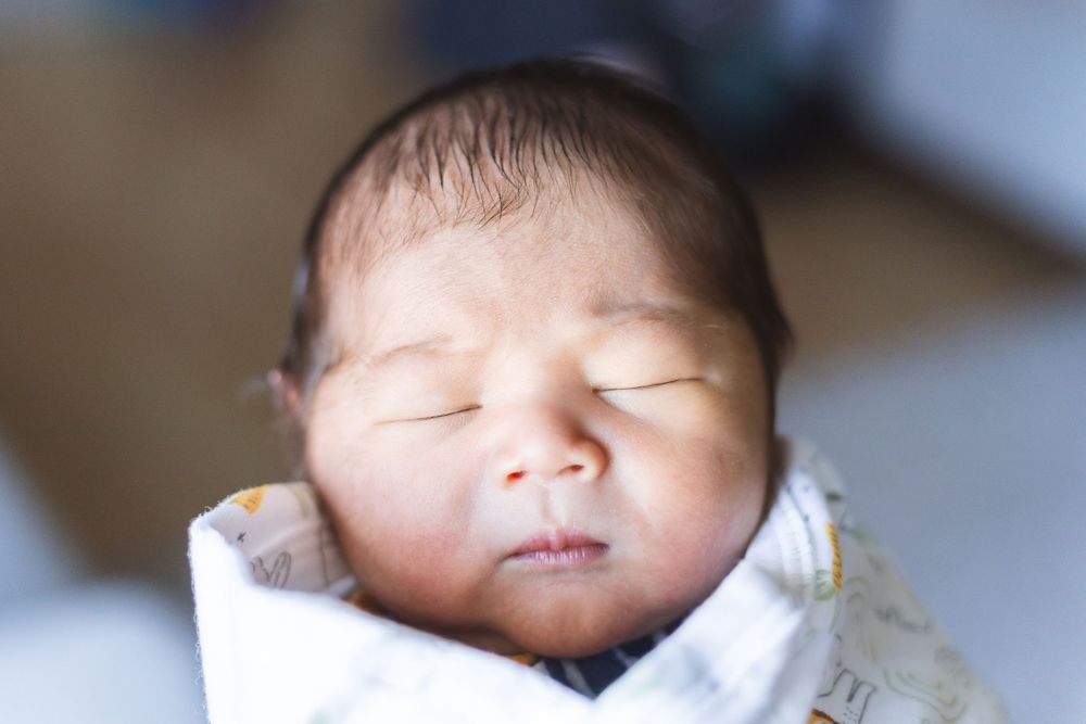 Sleeping baby in soft white blanket shown in close-up portrait series.