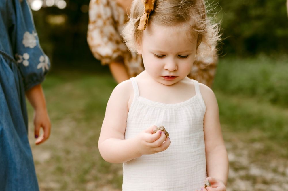 A close-up shot of a small child in a white dress examining something in their hand.