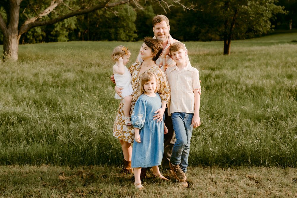 Family standing together in a sunlit meadow wearing coordinated casual outfits.