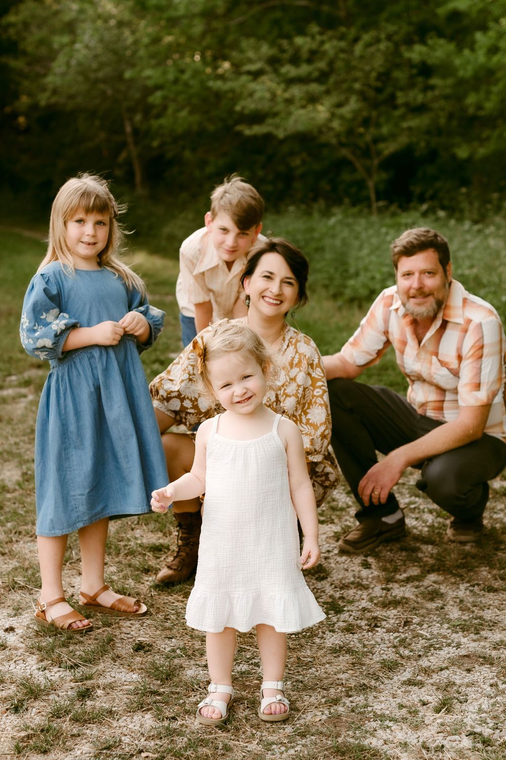 A sweet family portrait taken outdoors with natural scenery in the background.