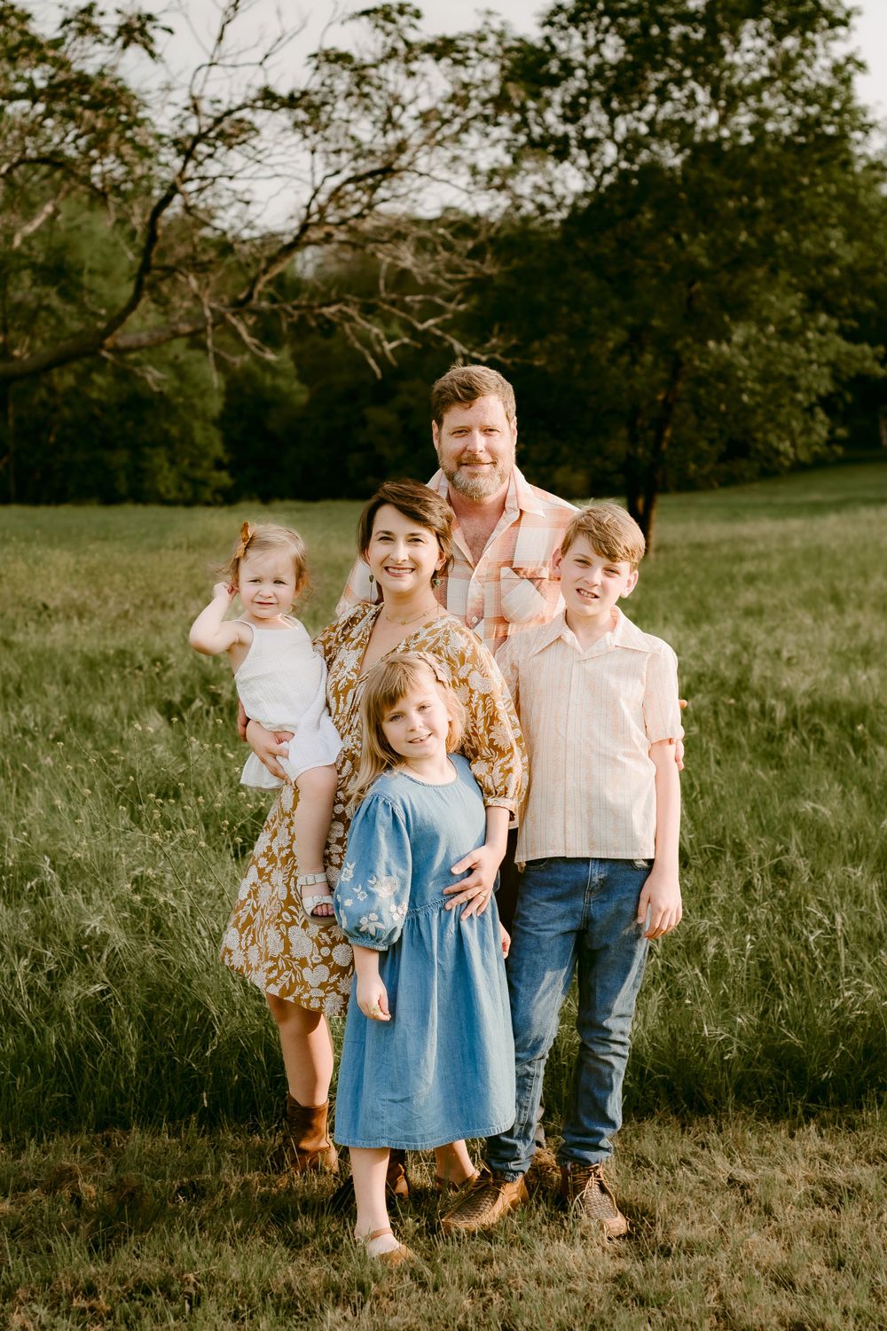 A group portrait of a family of five standing together in a grassy field during golden hour.