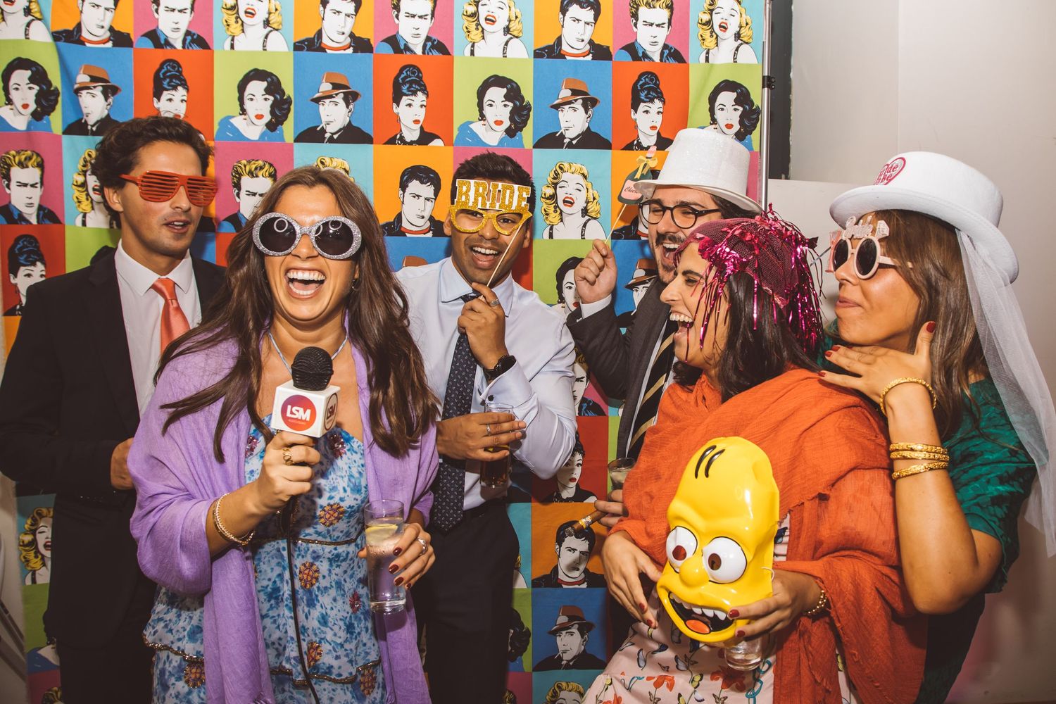 Wedding reception guests taking photos with colorful pop art style portraits on wall behind them.