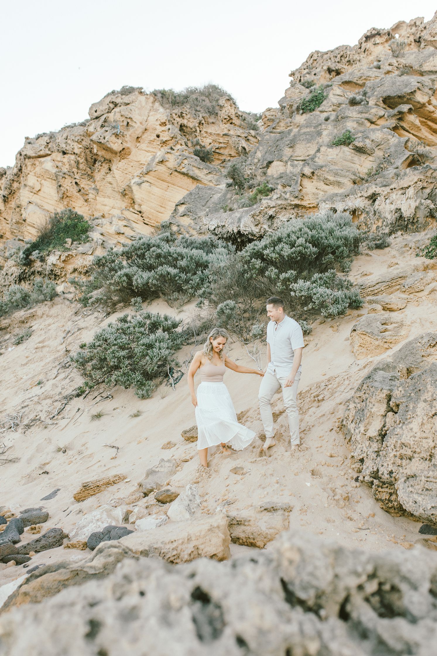 A couple descends a dramatic coastal cliff path during their romantic beach photoshoot.