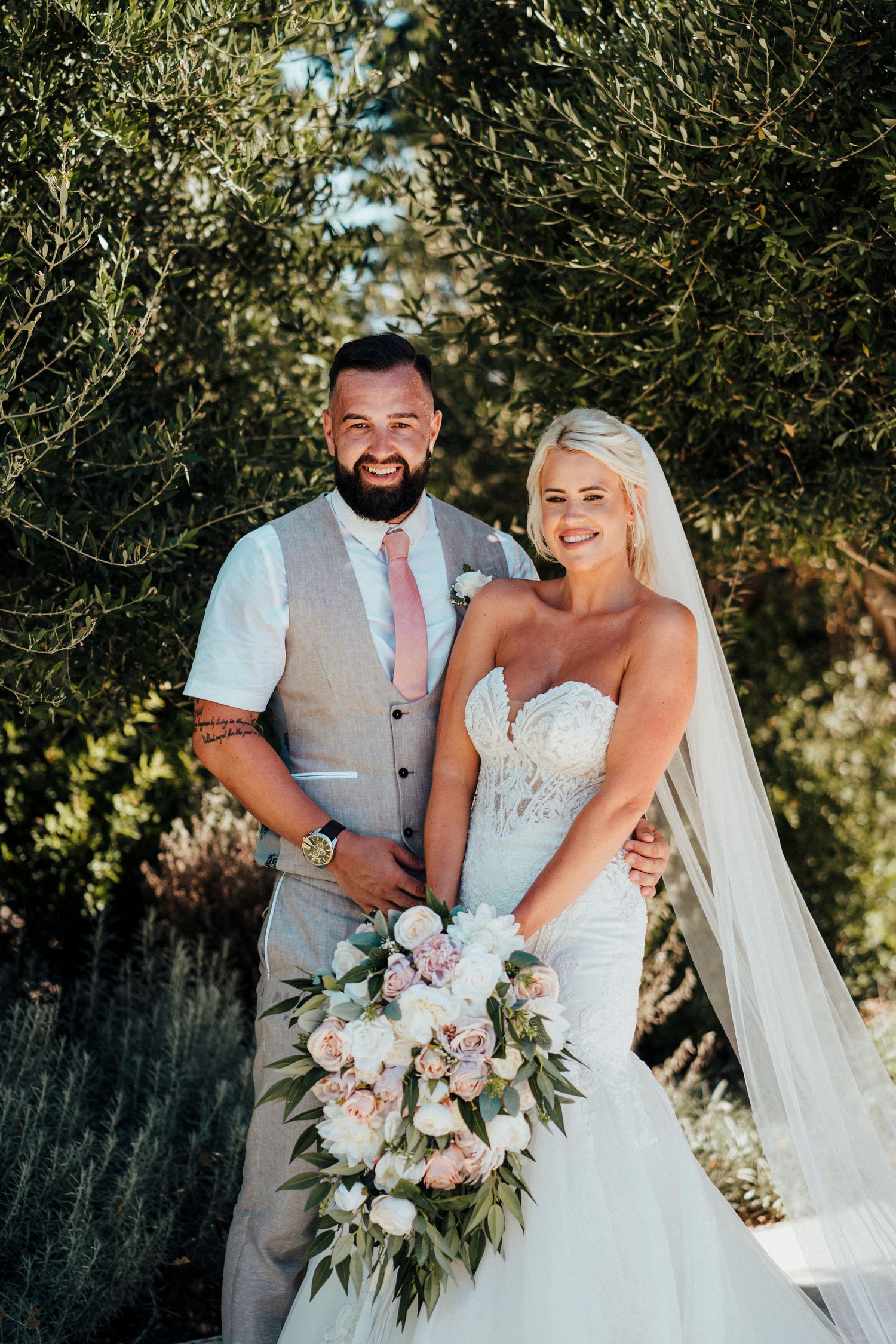 A wedding portrait among olive trees with a beautiful floral bouquet.