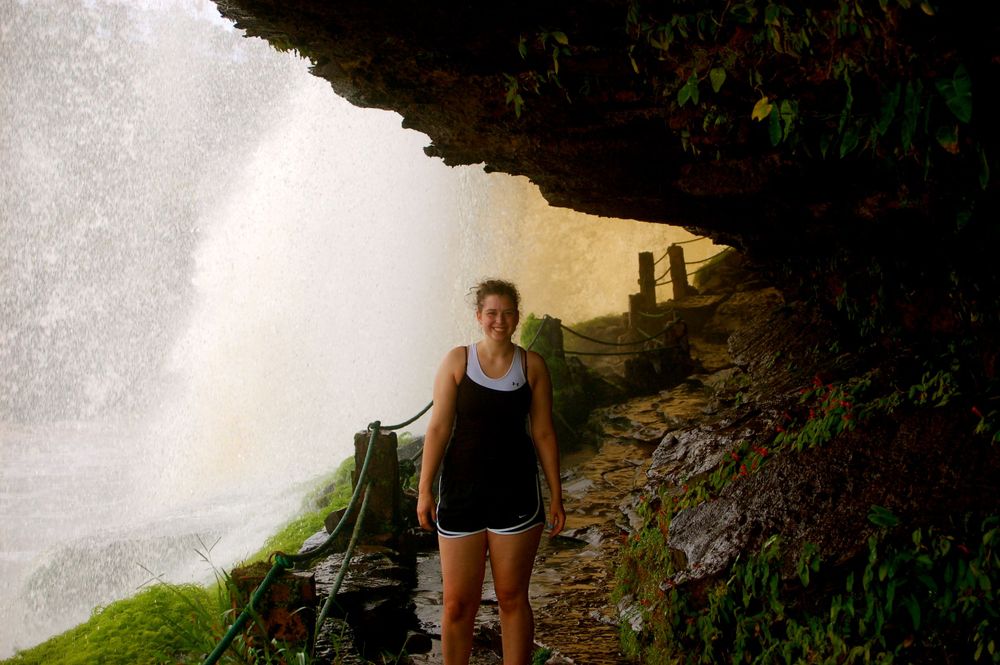 A scenic pathway leads behind a massive waterfall curtain in a rocky cave setting.