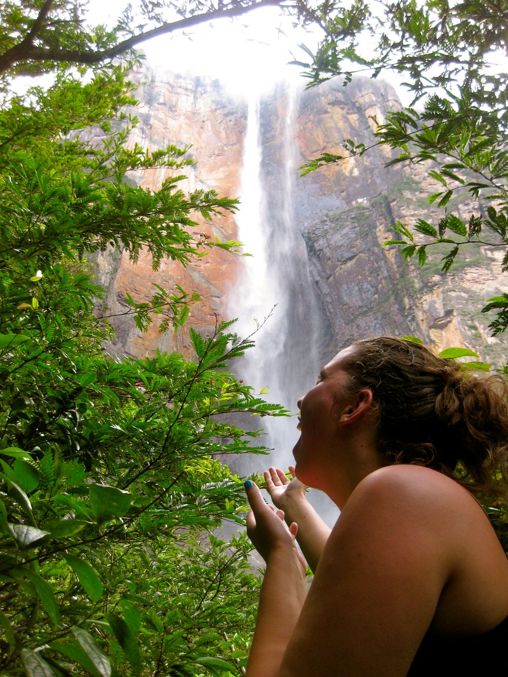 A tall waterfall plunges down dramatic orange cliffs framed by green foliage in a scenic landscape.