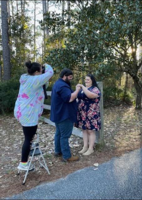 Behind the scenes photo of a photographer capturing an engagement session in a wooded setting.