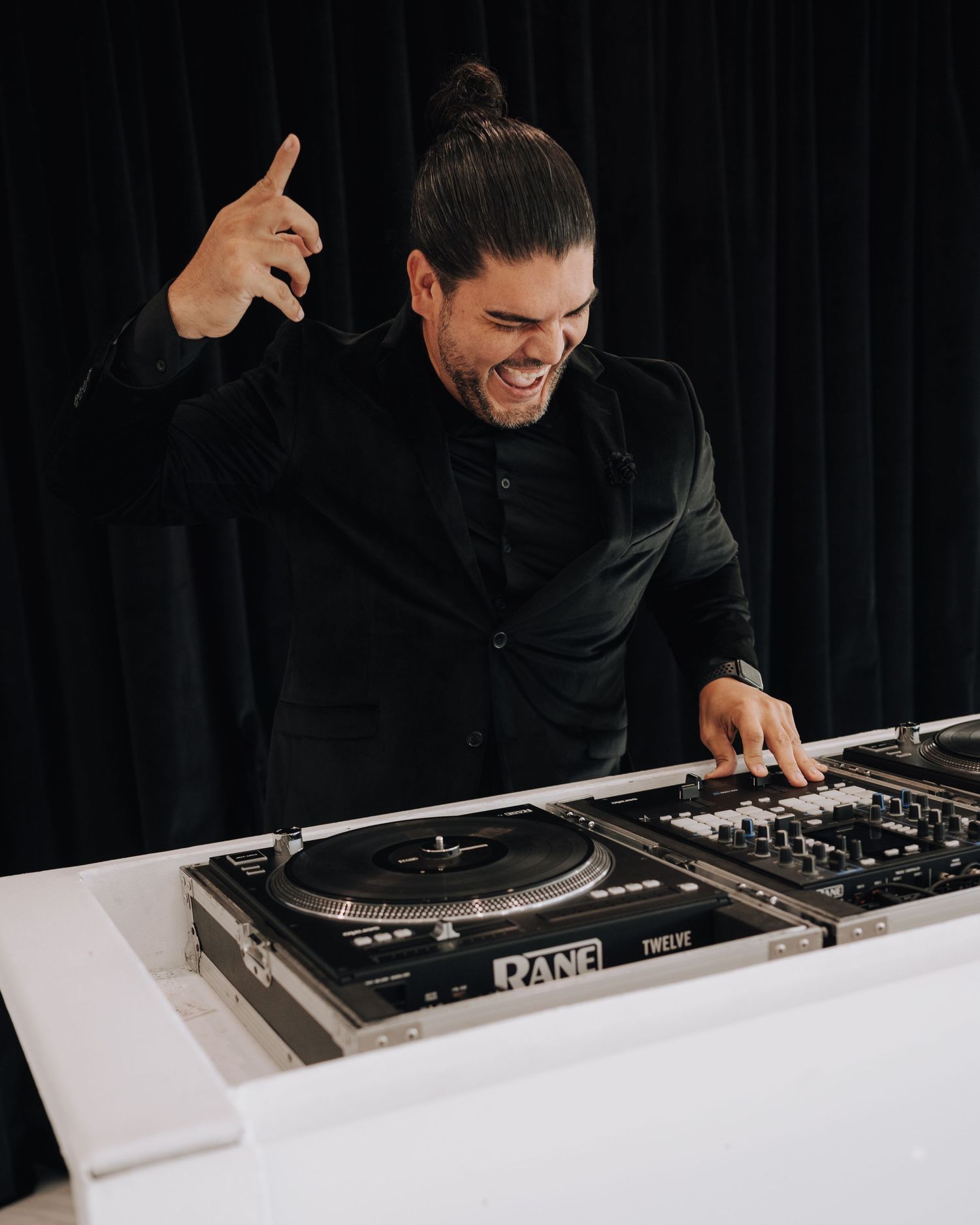 DJ performing at white modern booth against black backdrop during wedding reception.