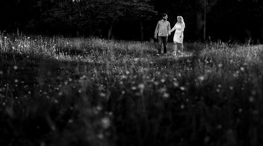 Black and white image of two people walking through a wildflower meadow.