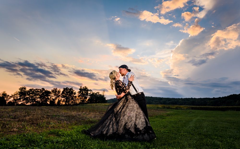 A couple embraces in a meadow during golden hour with dramatic clouds in the background.