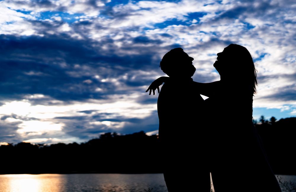 Dramatic silhouettes against a cloudy sky over water during sunset.