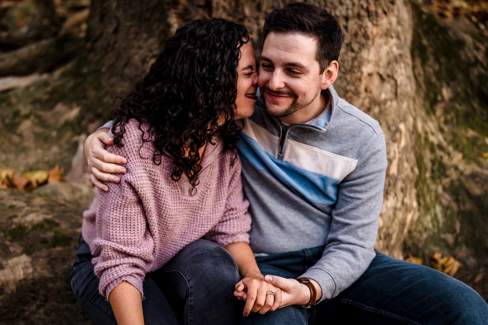 A couple shares an intimate moment while sitting against a large tree trunk.