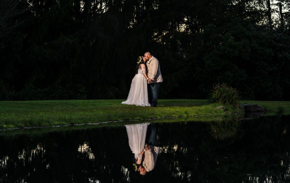 Couple embraces in romantic sunset silhouette against a wooded backdrop.