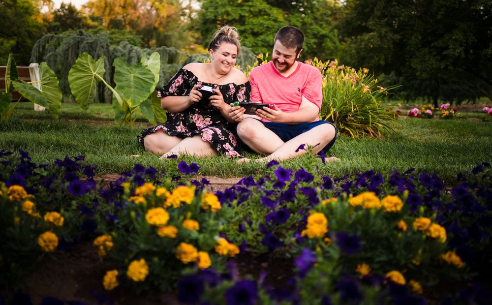 Couple sits together among vibrant yellow and purple flowers in a garden.