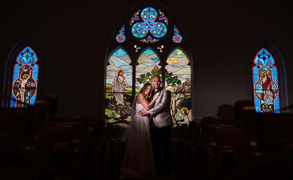 Colorful stained glass windows create dramatic lighting in a dark church interior.