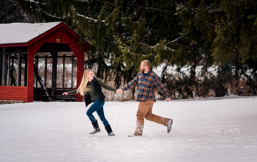 A snowy winter engagement session in front of a red barn.