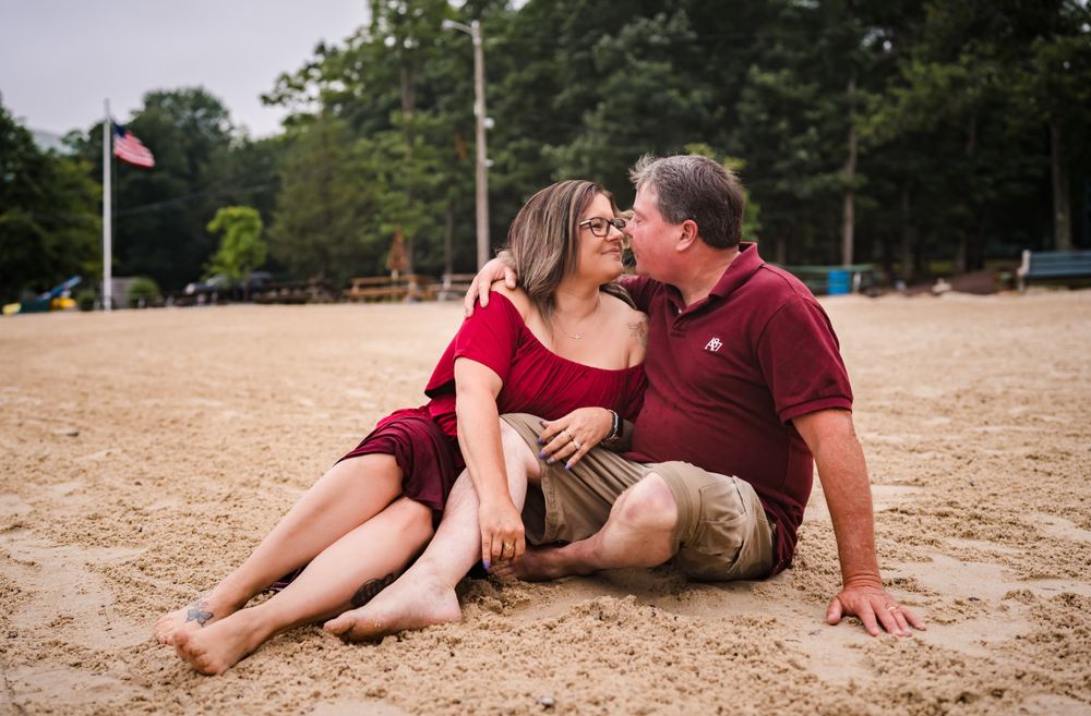 Couple in burgundy attire sharing intimate moment on sandy beach.