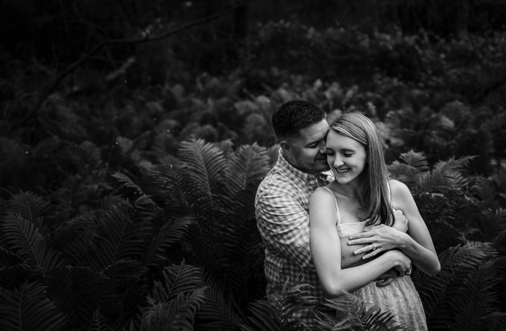 A couple embraces lovingly in a romantic outdoor setting with natural greenery in the background.