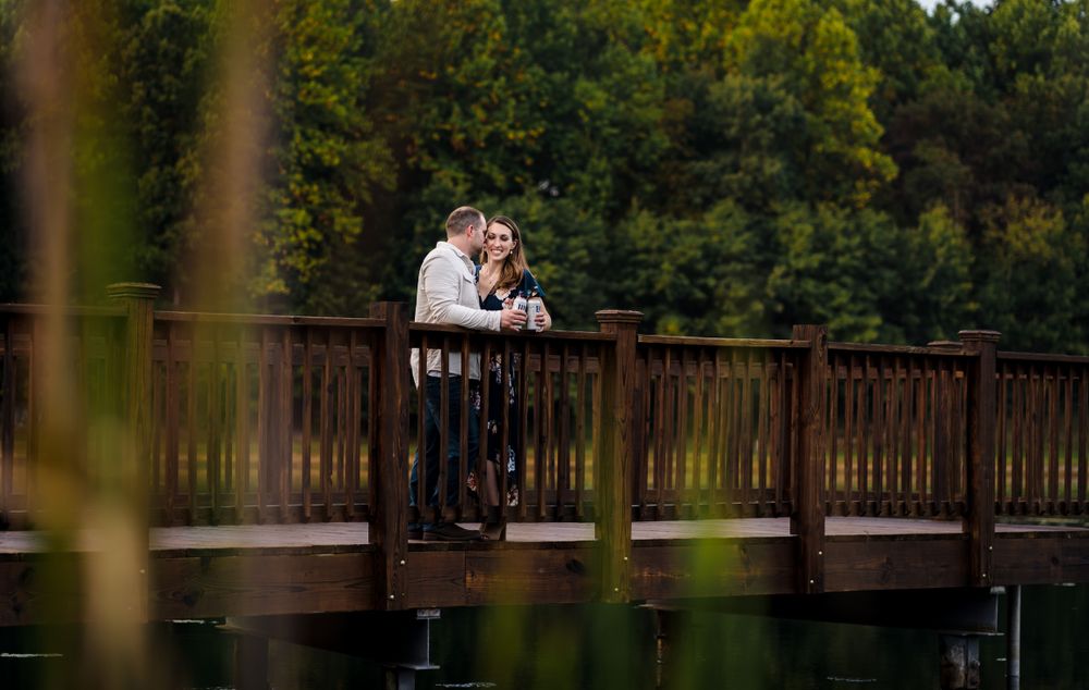 A couple shares an intimate moment on a wooden bridge surrounded by lush trees.
