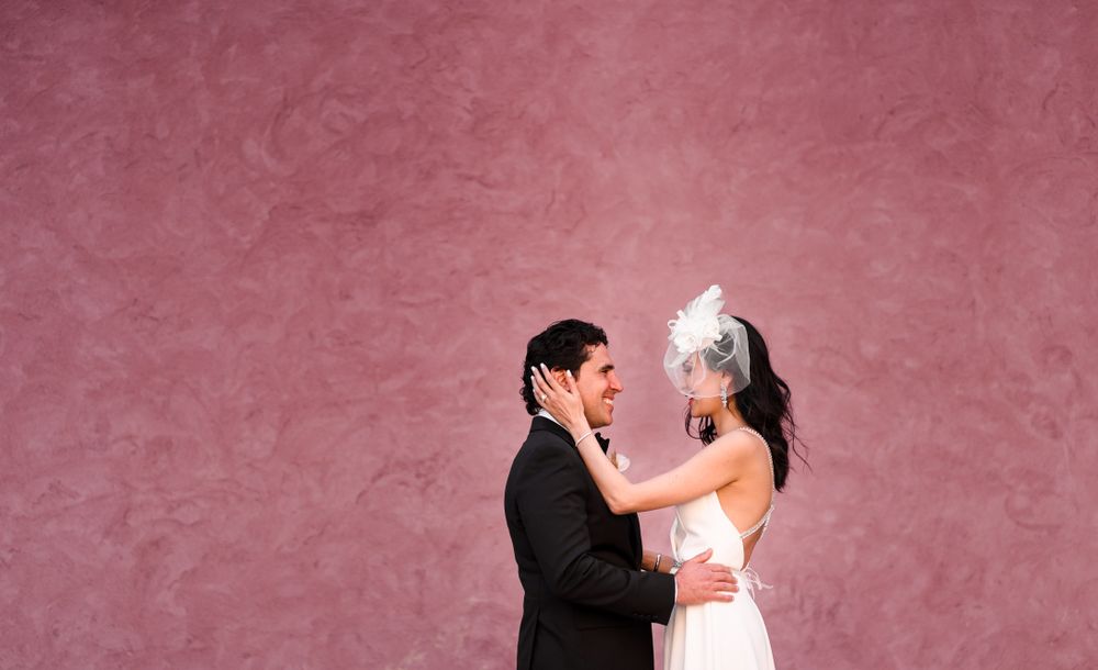 A couple poses romantically against a pink studio backdrop.
